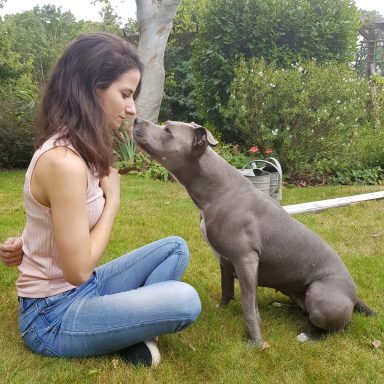 Une femme câline un chien dans un jardin verdoyant.
